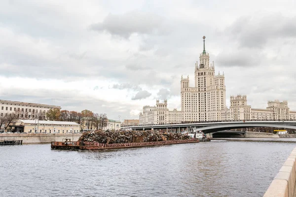 High-rise building in Empire style on Kotelnicheskaya embankment in Moscow and big barge ship with metal for recycling