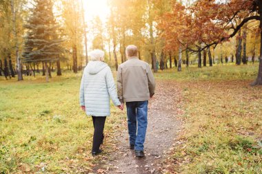 Sonbahar parkında yürüyen yaşlı çift.