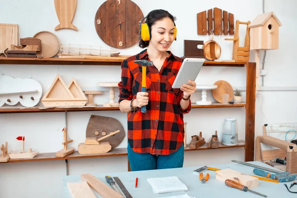 Funny woman with tablet pc and hammer in workshop. DIY concept — Stock Photo, Image