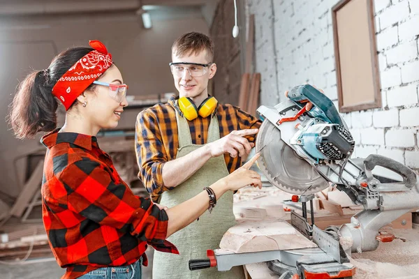 A male craftsman explains to a girl apprentice how to work with — Stock Photo, Image