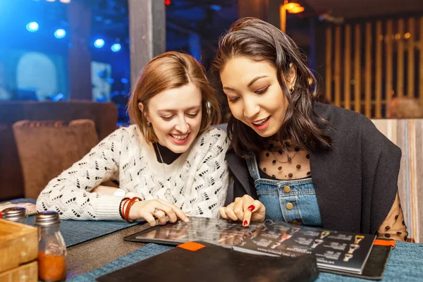 Dvě děvčata nejlepší kamarádi si vybírají jídlo a četbu v restauraci v nočním klubu. Koncepce stravování a vztahů — Stock fotografie
