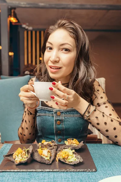 Mladá asijská žena pití čaje s tapas v restauraci — Stock fotografie