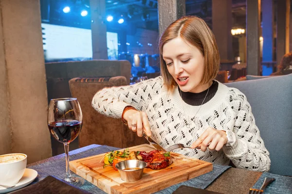 Woman eating meat steak and drinking wine in a restaurant in a nightclub