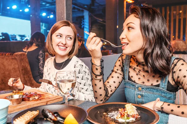 Dos amigas felices divirtiéndose juntas en el restaurante de la discoteca. comida, relaciones y concepto de estilo de vida . — Foto de Stock