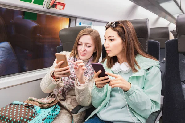 Two girlfriend girls ride the train in the subway and use their mobile phones — Stock Photo, Image