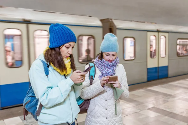 Two girls friends using smart phone application at the metro station — Stock Photo, Image