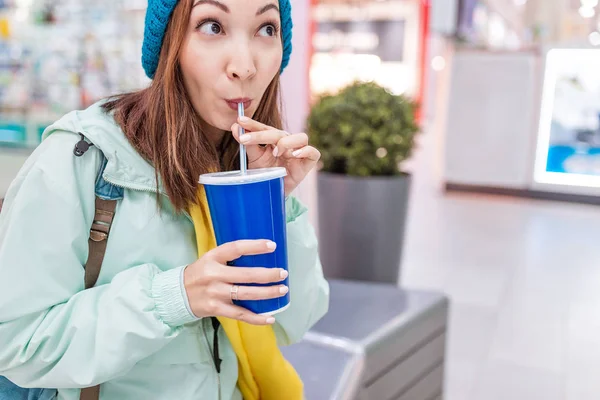 happy woman drinking soda with straw in a mall