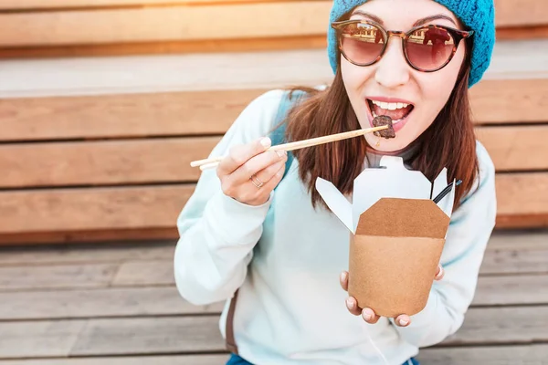 Moda asiática adolescente hipster chica come oriental wok fideos con palillos. Concepto de almuerzo y recipientes naturales para llevar hechos de papel —  Fotos de Stock