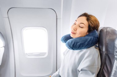 Asya kız uyku, bir maske ve bir yastık ile pencereden yakın uçakta onu koltukta uyuyan. Konfor ve jetlag ile seyahat kavramı
