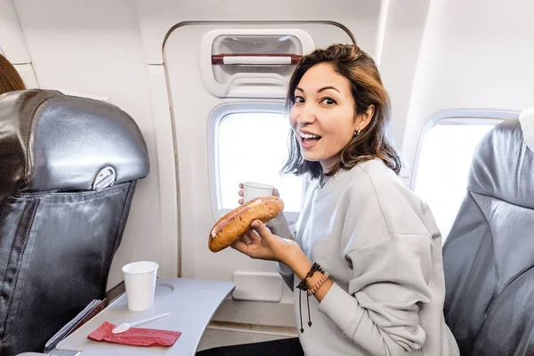 Uçak seyahat ederken kahve fincan ile sandviç yeme mutlu Asya kadın — Stok fotoğraf