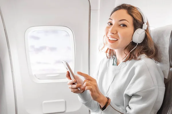 Happy Asian Girl ze słuchawkami słuchanie muzyki przez smartfona podczas podróży samolotem — Zdjęcie stockowe