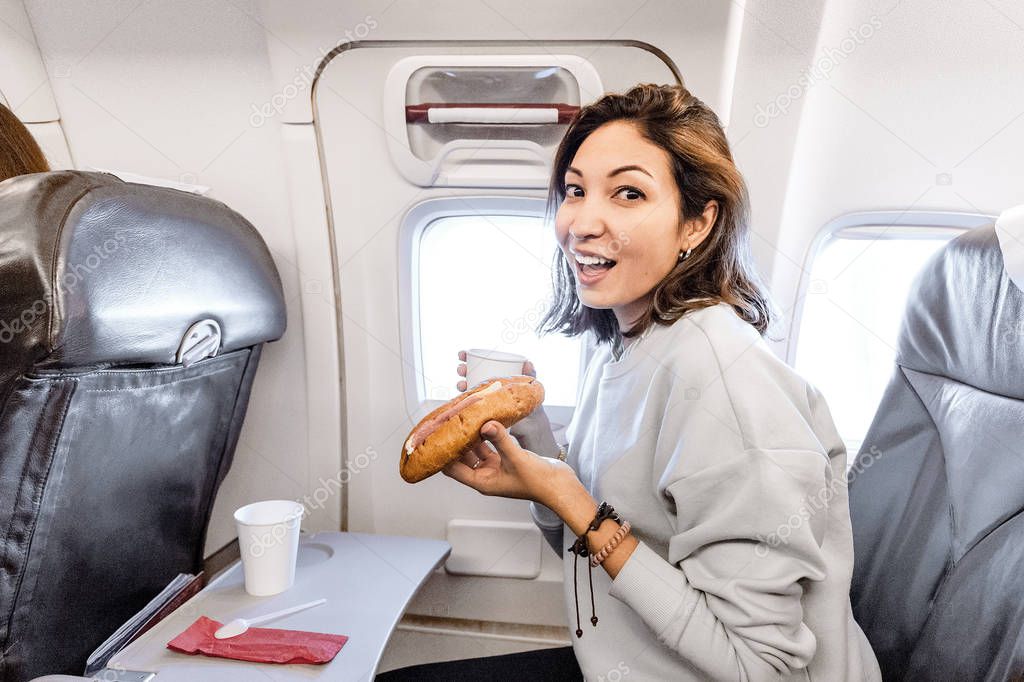 Happy asian Woman eating sandwich with cup of coffee while travelling on airplane