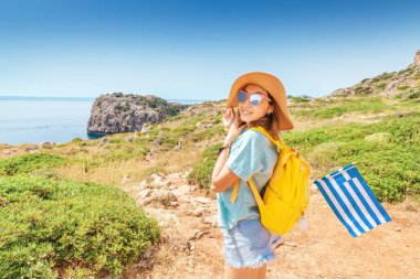 Yunanistan 'da yaya yolu ile seyahat eden sırt çantası ve Yunan bayrağı ile mutlu kadın turist