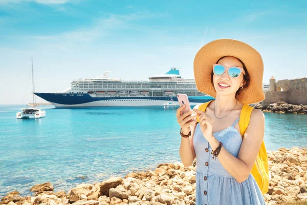 Asian woman traveler uses phone on the background of a large cruise liner. The concept of coverage, roaming and pay for the resort online