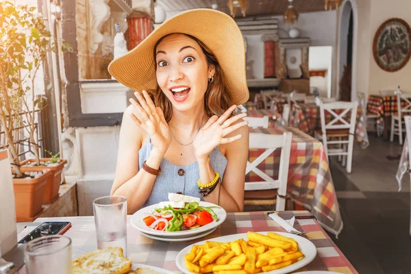 Щаслива Азіатська жінка в Big Hat з їжею з грецьким салатом Horiatiki в ресторані. Концепція Греції кухня — стокове фото