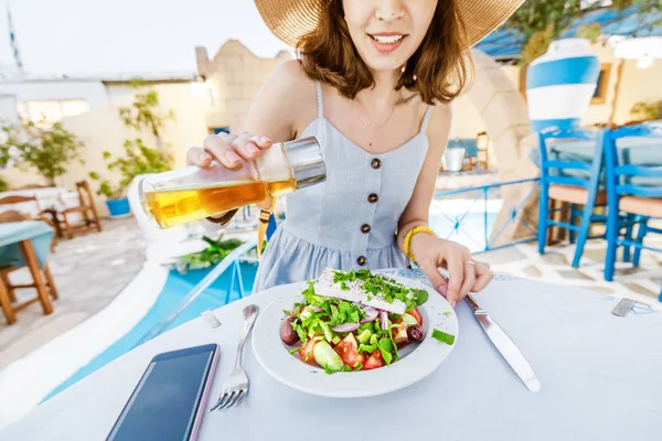 Ung elegant pige i restauranten krydderier salat med olivenolie. Begrebet græsk køkken og friske grøntsager - Stock-foto