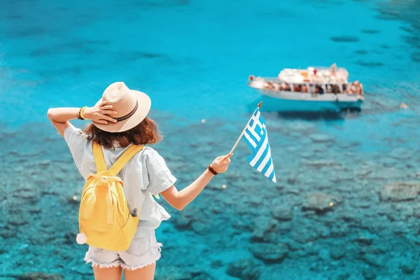 Šťastná dívka s řeckou vlajkou na pozadí výletních člunů v krásném zálivu Středozemního moře. Koncepce cestování a dopravy v Řecku — Stock fotografie