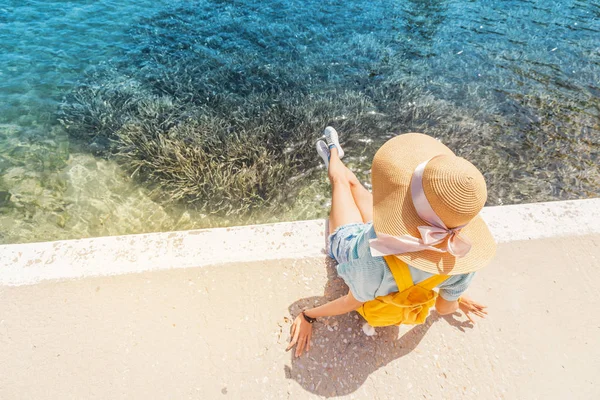 Chica viajera en un gran sombrero descansando y relajándose en el muelle cerca del hermoso mar de azul. Composición minimalista — Foto de Stock