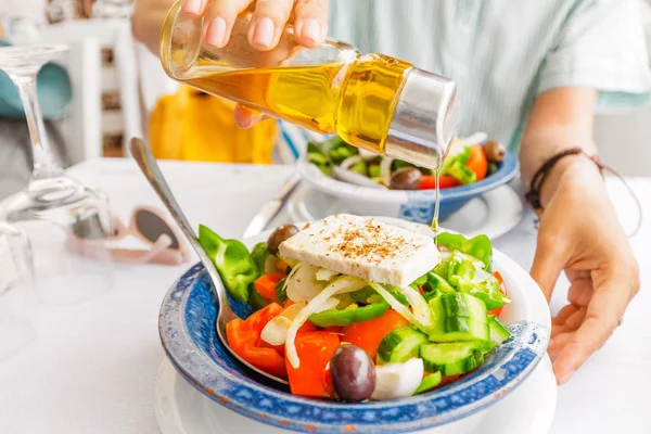 Woman pouring delicious Olive oil into greek salad in restaurant. Healthy food and vegetarian concept — Stock Photo, Image