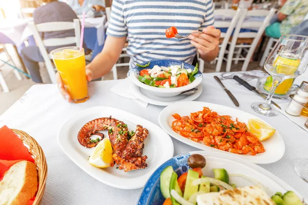Close-up of a man eating delicious seafood - shrimp and octopus grilled and vegetable salad. The concept of Mediterranean cuisine and healthy food