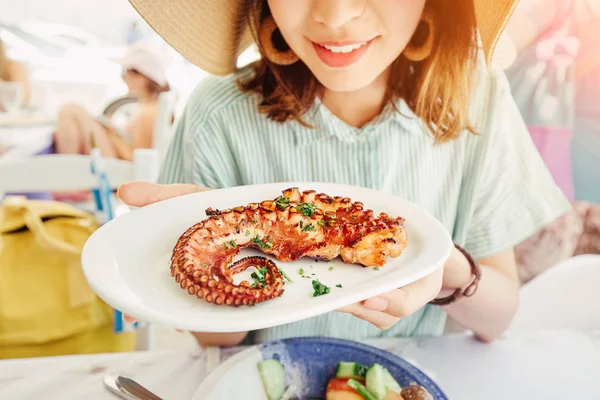 Happy asian woman in hat eating delicious grilled octopus in seafood restaurant. Delicacy and healthy gourmet cuisine — Stock Photo, Image