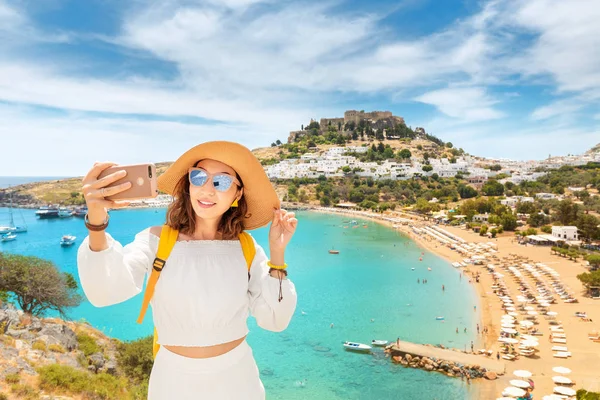 Mulher jovem e feliz turista tirar foto selfie em seu smartphone com vista para uma praia de areia e cidade velha. Conceito de férias e viagens — Fotografia de Stock