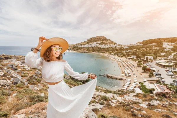 Glückliche asiatische Frau reist in Griechenland. Spaß am atemberaubenden Blick auf den Badeort und die Altstadt von Lindos auf dem Berg — Stockfoto