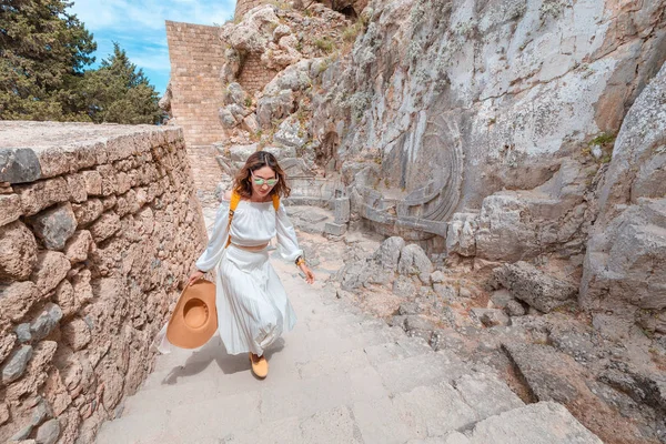 린도스 아크로폴리스의 역사및 고고학 유적지에서 배낭을 걷는 행복한 아시아 여행자. 그리스의 관광 명소와 고대 건축물 — 스톡 사진