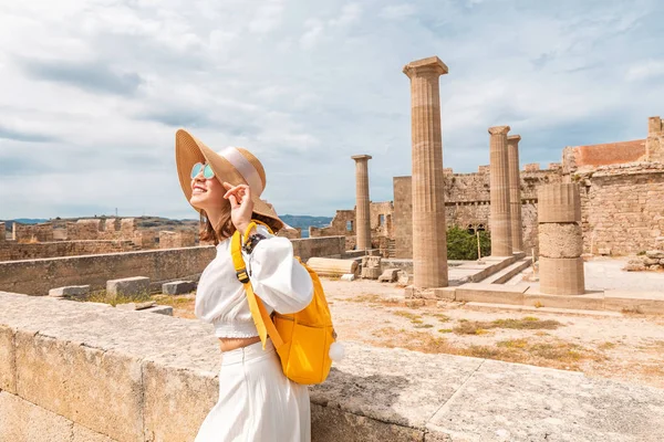 Feliz viajero asiático con mochila caminando en sitio histórico y arqueológico en la Acrópolis de Lindos. Atracción turística y arquitectura antigua en Grecia — Foto de Stock