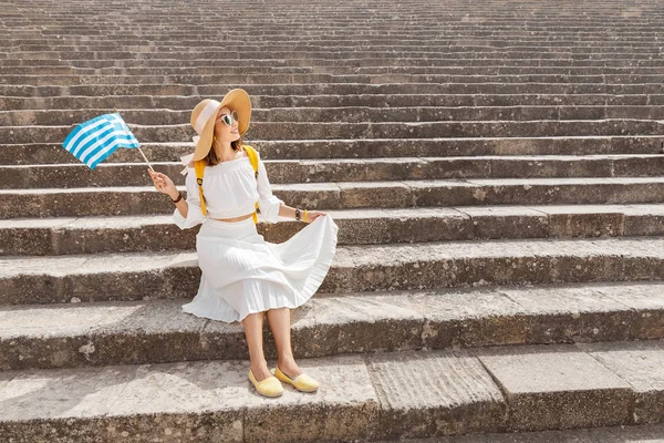 Young traveler woman with greek flag at the ancient greek ruins. Tourism in Greece concept