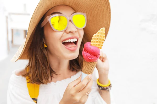 Щаслива азіатка в капелюсі і сонцезахисних окулярах їсть смачний десерт морозива в білому місті — стокове фото