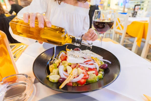 Woman pouring olive oil in greek fresh salad in restaurant — Stock Photo, Image