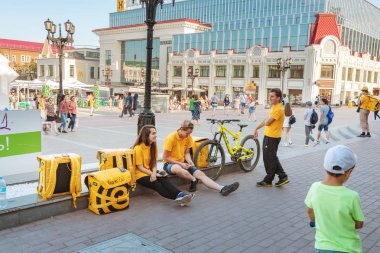 22 JUNE 2019, UFA, RUSSIA: Workers of the Yandex Food delivery service resting on a city square clipart