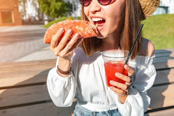 Happy asian girl eating taco outside and drinking beverage. Mexican fastfood cuisine. Tasty and spicy snack in park