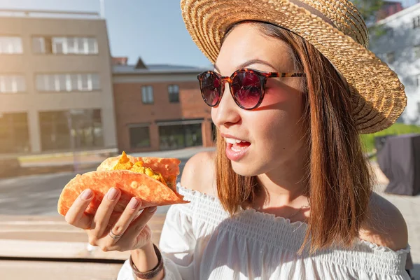 Happy asian girl eating taco outside. Mexican fastfood cuisine. Tasty and spicy snack in park