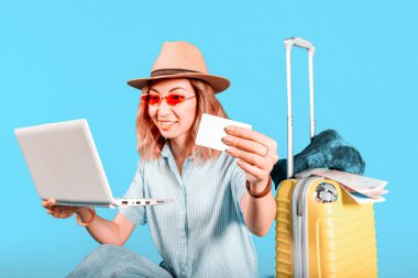 Mutlu bir kız bir dizüstü bilgisayar ve Banka kredi kartı kullanarak bir turist gezisi veya tur satın alır. Yolculuk e-ticaret konsepti. Renkli bir arka plan üzerinde Studio Çekim.