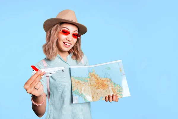 Щаслива азіатська жінка з картою та іграшковим літаком у студії на кольоровому фоні — стокове фото