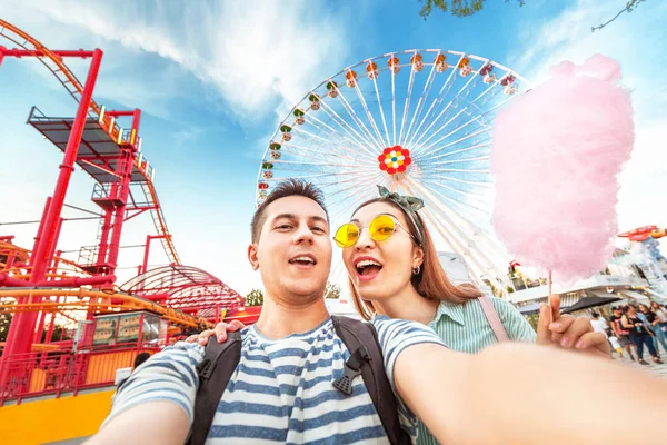 Amar a la pareja de razas mixtas abrazando y comiendo algodón de azúcar y tomando selfie durante el fin de semana en el parque de atracciones. Fecha y relación — Foto de Stock