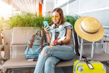 Havaalanı veya tren istasyonu terminal salonunda beklerken ve otururken akıllı telefon uising genç asyalı kadın yolcu