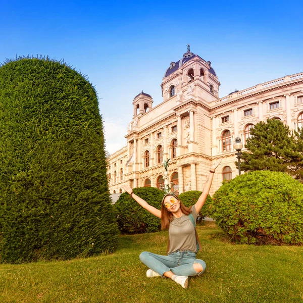 Happy young woman sitting on a green lawn near historical architecture building in Vienna city, Austria. Travel and student lifestyle concept — Stock Photo, Image