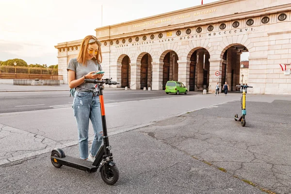 Mujer usando smartphone y alquilando scooter eléctrico moderno con una aplicación. Concepto de transporte urbano —  Fotos de Stock