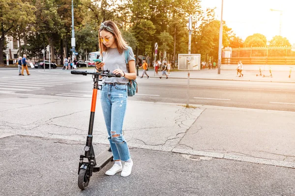 Donna che utilizza smartphone e noleggio scooter elettrico moderno con un'applicazione. Concetto di trasporto urbano — Foto Stock