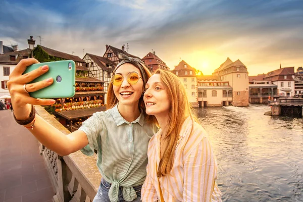 Fransa'nın Strazburg kentinde ki Saint Martin köprüsünde görkemli gün batımı nda selfie fotoğrafı çeken mutlu arkadaşlar. Gençler ve öğrenciler için seyahat konsepti