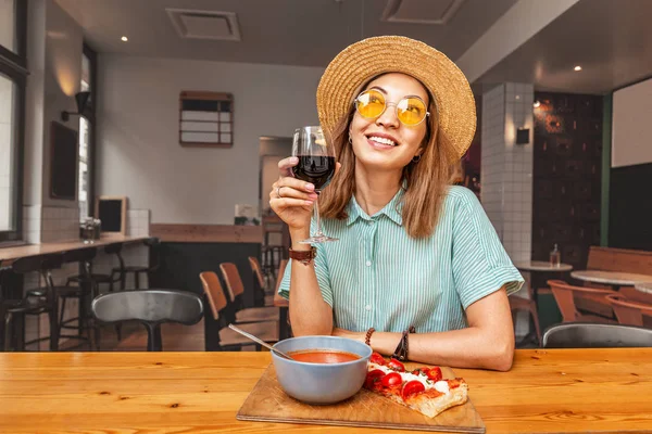 Счастливая азиатка ест в ресторане и пьет красное вино. Итальянская или испанская кухня — стоковое фото
