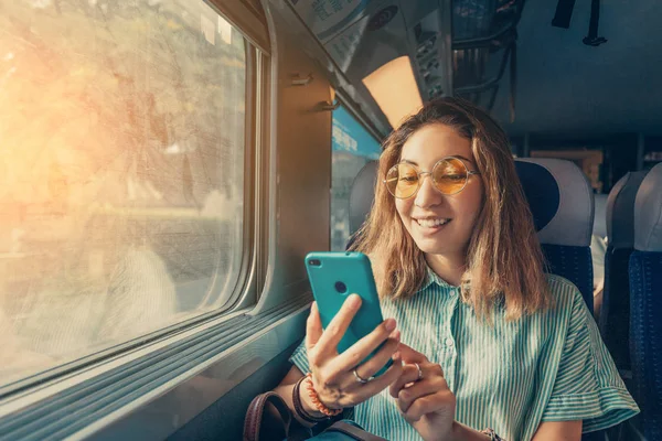 Happy Asian girl using transport application on smartphone while travelling by high speed train — Stock Photo, Image