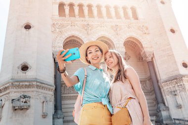 Fransa'nın Lyon kentindeki Notre Dame de Fourviere Katedrali önünde selfie çeken iki mutlu kadın arkadaş. Turizm ve din kavramı