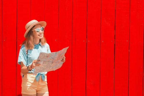 Happy asian tourist girl reading map on bright colorful red freshly painted wooden Board background