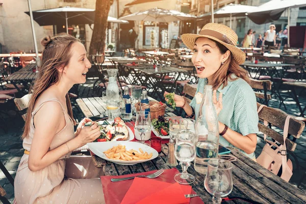 Two happy girls friends have a fun conversation and talking while a little meal in a terrace restaurant outdoors — Stock Photo, Image