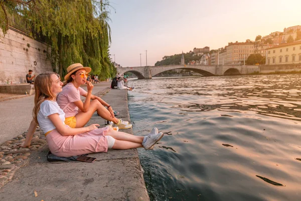 Dois felizes caucasiano e asiático meninas amigos encontrando grande pôr do sol em um rio Saone na cidade de Lyon. Viagens e estilo de vida em França — Fotografia de Stock