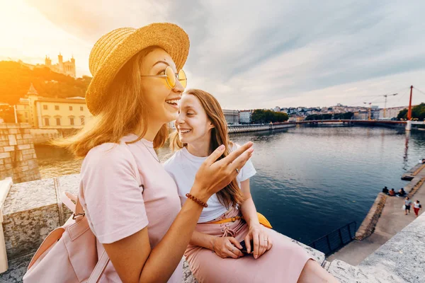 Дві щасливі кавказькі і Азіатські дівчата друзі засідання великий захід сонця на річці Saone в місті Ліон. Подорожі та спосіб життя у Франції — стокове фото